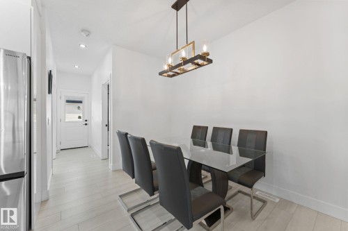 Dining area featuring a modern linear chandelier, light wood-finish flooring, and recessed lighting - 3606 42 Avenue, Beaumont, AB 