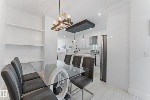 Dining area with a modern glass-top table, sculptural base, and built-in wall shelving - 3606 42 Avenue, Beaumont, AB 