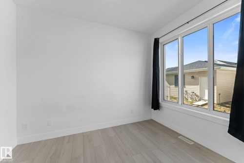 Bright room with a large multi-pane window, light wood-finish flooring, white baseboards, and neutral wall paint - 3606 42 Avenue, Beaumont, AB 
