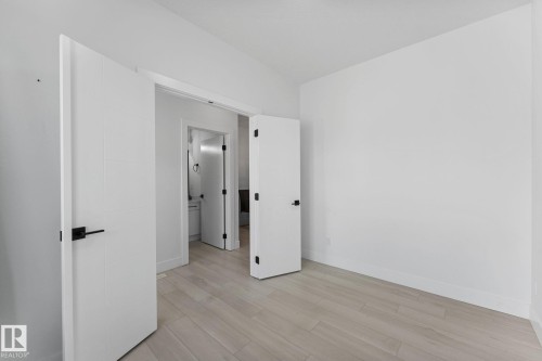 Room featuring wood-finish flooring, crisp white walls, and contemporary slab doors with matte black hardware - 3606 42 Avenue, Beaumont, AB 