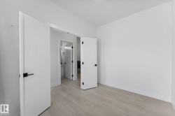 Room featuring wood-finish flooring, crisp white walls, and contemporary slab doors with matte black hardware - 