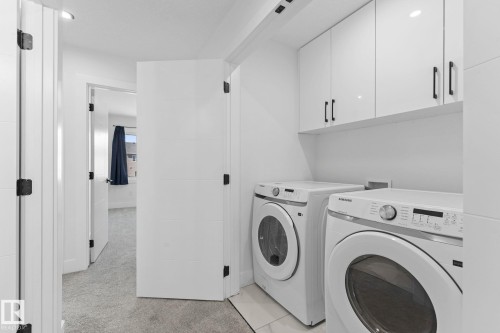 Dedicated laundry area featuring white gloss cabinetry with dark hardware, white tile flooring, and recessed lighting - 3606 42 Avenue, Beaumont, AB 