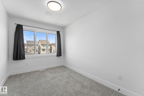 Neutral-toned room featuring a triple-pane window, light gray carpet, and a flush-mount ceiling light - 3606 42 Avenue, Beaumont, AB 