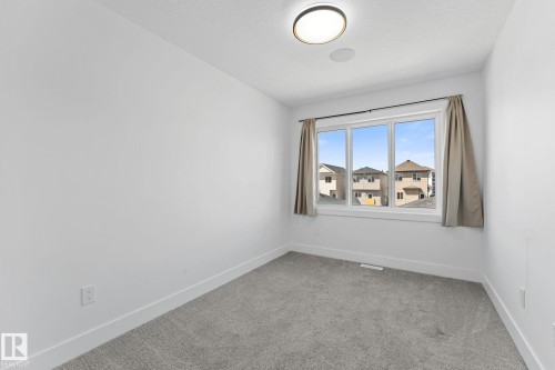 Room featuring a large multi-pane window, neutral-toned curtains, gray carpet flooring, clean white walls, and a contemporary flush-mount ceiling light - 3606 42 Avenue, Beaumont, AB 
