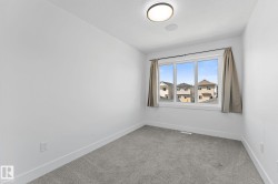 Room featuring a large multi-pane window, neutral-toned curtains, gray carpet flooring, clean white walls, and a contemporary flush-mount ceiling light - 