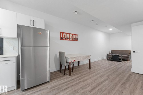 Open-concept living space featuring wood-finish flooring, white cabinetry with dark hardware, a stainless steel refrigerator, and recessed lighting - 3606 42 Avenue, Beaumont, AB 