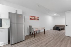 Open-concept living space featuring wood-finish flooring, white cabinetry with dark hardware, a stainless steel refrigerator, and recessed lighting - 