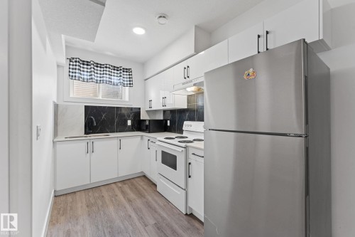 Modern kitchen featuring white cabinetry, a stainless steel refrigerator, white electric range, and wood-finish flooring - 3606 42 Avenue, Beaumont, AB 