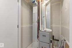 Utility closet featuring a furnace with visible ductwork and piping, drywall-finished walls, and a white interior door - 