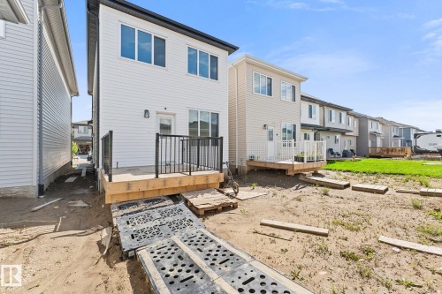 Rear exterior featuring white horizontal siding, a wooden deck with black railings, a glass sliding door, and multiple windows - 3606 42 Avenue, Beaumont, AB 