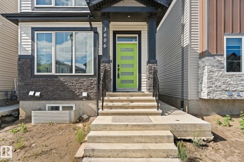 Modern exterior featuring a vibrant green front door, contrasting dark trim, stacked stone accents, and white horizontal siding - 3606 42 Avenue, Beaumont, AB 