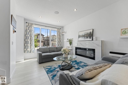Bright living space featuring wood-finish flooring, a contemporary electric fireplace with a marble-look surround, and recessed ceiling lights - 3606 42 Avenue, Beaumont, AB 