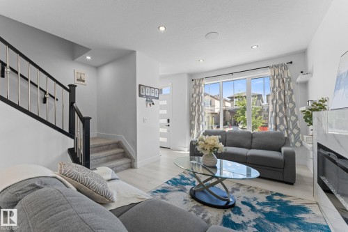 Expansive living area featuring light wood-finish flooring, recessed lighting, a modern fireplace with a marble-finish surround, and a contemporary staircase with black and silver railings - 3606 42 Avenue, Beaumont, AB 