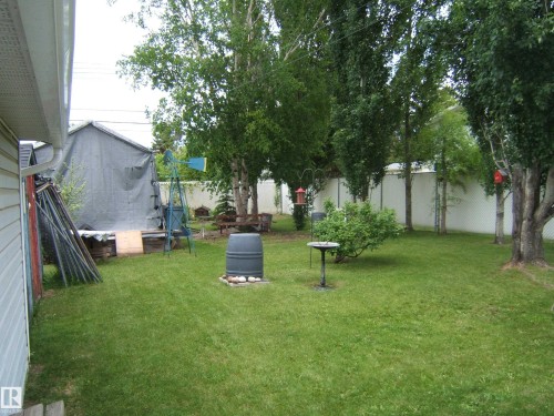 Expansive rear yard featuring a manicured lawn, mature trees, and a white privacy fence - 4606 51 Avenue, Two Hills, AB 