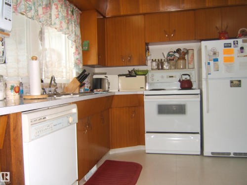 Kitchen featuring wood-finish cabinetry, white countertops, a white dishwasher, a white electric range, and a white refrigerator - 4606 51 Avenue, Two Hills, AB 