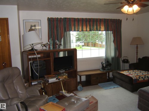 Living area featuring a large window with white trim, a ceiling fan with light fixture, and light-toned carpeting - 4606 51 Avenue, Two Hills, AB 