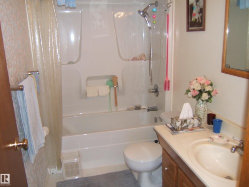 Bathroom featuring a white bathtub and shower surround, a chrome showerhead with an attached handheld sprayer, and a wood-finish vanity with an integrated sink and chrome faucet - 4606 51 Avenue, Two Hills, AB 