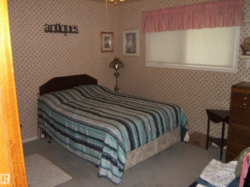 Bedroom featuring patterned wallpaper, carpet flooring, and a window with blinds and a fabric valance - 4606 51 Avenue, Two Hills, AB 