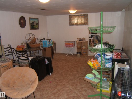 Room featuring a drop-ceiling, wall-mounted light fixtures, paneling on one wall, and carpet flooring - 4606 51 Avenue, Two Hills, AB 