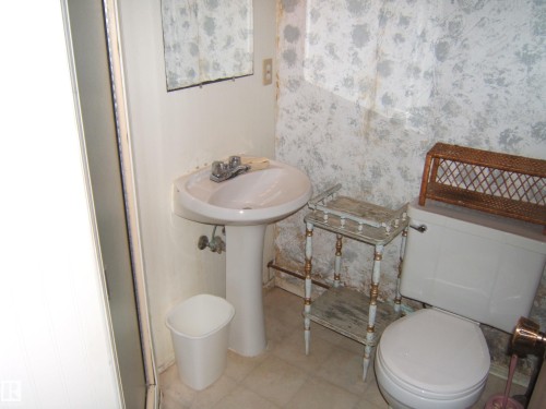 White pedestal sink with a dual-handle faucet and an oval-shaped toilet - 4606 51 Avenue, Two Hills, AB 