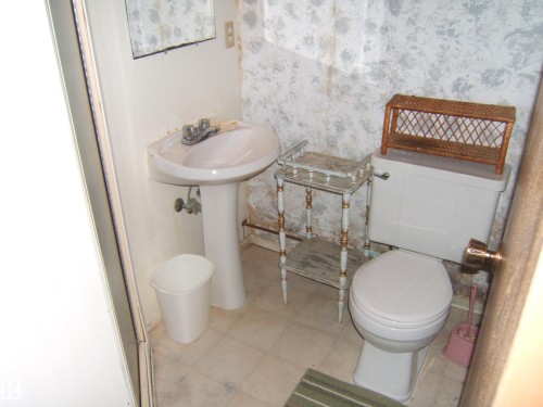 Pedestal sink with chrome faucet, toilet, and light-toned floor tiles - 4606 51 Avenue, Two Hills, AB 