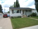 Single-story residence featuring light-colored siding, a dark shingle roof, and a mature front lawn - 4606 51 Avenue, Two Hills, AB 