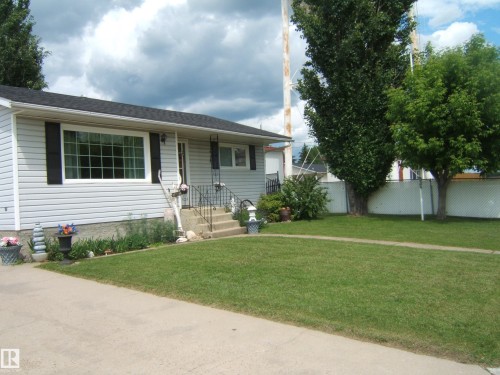 Single-story residence featuring light-colored siding, a dark shingled roof, and a prominent front picture window with dark shutters - 4606 51 Avenue, Two Hills, AB 
