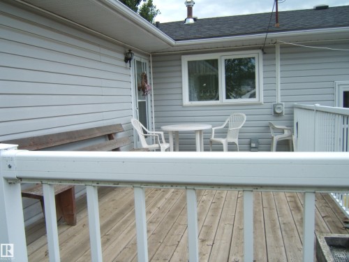 Exterior wood deck with white railing, featuring light gray horizontal siding, a sliding glass door, and a white-framed window - 4606 51 Avenue, Two Hills, AB 