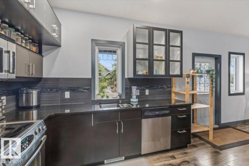 Modern kitchen featuring dark wood-finish cabinetry, stainless steel appliances, a double basin sink, and granite-look countertops - 3 7210 96 Street, Edmonton, AB - Indoor Photo Showing Kitchen With Double Sink