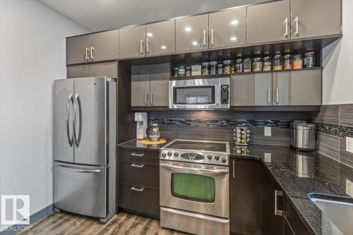 Modern kitchen featuring stainless steel appliances, dark wood-finish cabinetry, granite countertops, a tiled backsplash, and wood-finish flooring - 3 7210 96 Street, Edmonton, AB - Indoor Photo Showing Kitchen With Stainless Steel Kitchen With Upgraded Kitchen