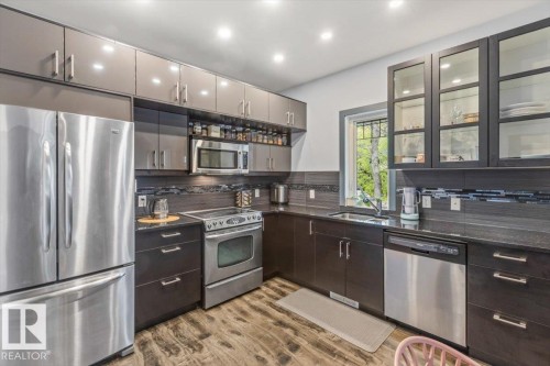 Modern kitchen featuring dark wood-finish base cabinetry, light grey upper cabinetry, stainless steel appliances, dark countertops, and wood-finish flooring - 3 7210 96 Street, Edmonton, AB - Indoor Photo Showing Kitchen With Stainless Steel Kitchen With Double Sink
