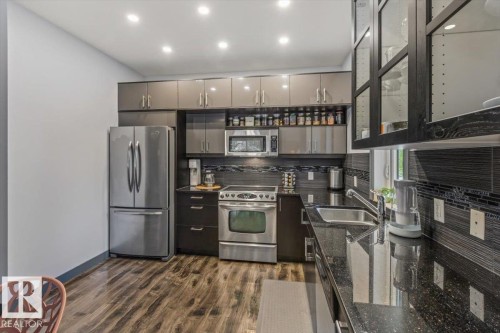 Contemporary kitchen featuring stainless steel appliances, dark wood-finish flooring, recessed lighting, and a dark stone countertop with an integrated sink - 3 7210 96 Street, Edmonton, AB - Indoor Photo Showing Kitchen With Stainless Steel Kitchen With Double Sink With Upgraded Kitchen
