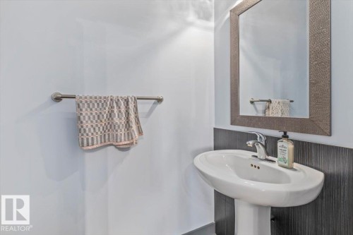 Pedestal sink with a chrome faucet, framed mirror, and dark wood-finish wainscoting - 3 7210 96 Street, Edmonton, AB - Indoor Photo Showing Bathroom