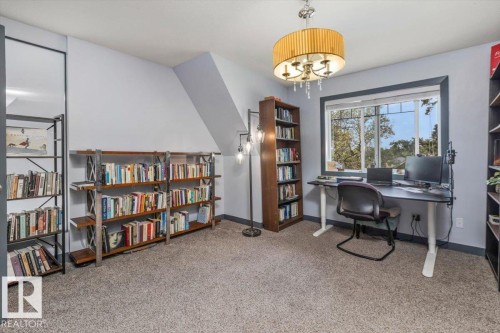 Carpeted room featuring a large window with exterior views, a contemporary chandelier, and built-in shelving - 3 7210 96 Street, Edmonton, AB - Indoor Photo Showing Office
