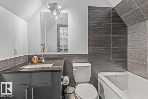 Contemporary bathroom featuring a white bathtub, toilet, and vanity with a dark countertop - 3 7210 96 Street, Edmonton, AB - Indoor Photo Showing Bathroom