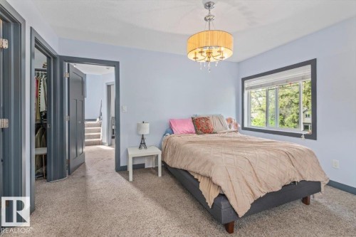 Carpeted room featuring light blue walls, dark trim, a window with blinds, and a drum-style chandelier - 3 7210 96 Street, Edmonton, AB - Indoor Photo Showing Bedroom