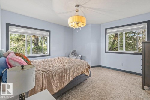 Carpeted room featuring two large windows with dark trim, a drum-style chandelier with decorative crystals, and light blue walls - 3 7210 96 Street, Edmonton, AB - Indoor Photo Showing Bedroom