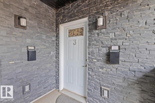 Entryway featuring stacked stone siding, white paneled door with decorative glass insert, and built-in mailboxes - 3 7210 96 Street, Edmonton, AB - Outdoor