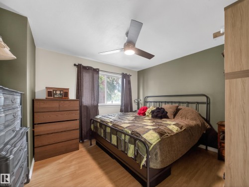 Spacious room featuring wood-finish flooring, a ceiling fan with integrated lighting, and a window with dark drapery - 10809 150 Street, Edmonton, AB 