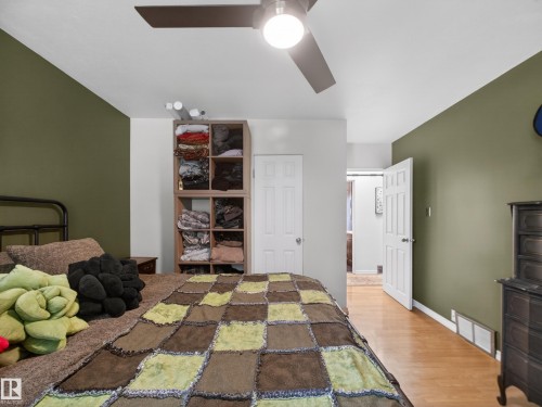 Bedroom featuring a ceiling fan with integrated lighting, wood-finish flooring, and a multi-toned accent wall - 10809 150 Street, Edmonton, AB 