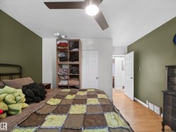 Bedroom featuring a ceiling fan with integrated lighting, wood-finish flooring, and a multi-toned accent wall - 