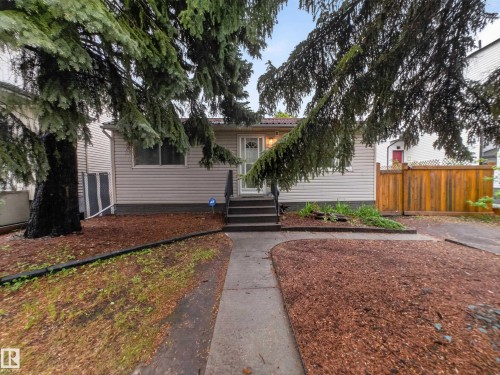 Single-story exterior with light-colored siding, a dark metal roof, and a concrete walkway leading to the entrance - 10809 150 Street, Edmonton, AB 