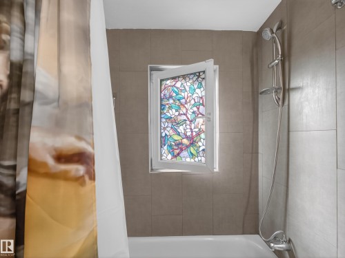 Bathtub with a decorative stained glass window and light-toned tile surround - 10809 150 Street, Edmonton, AB 