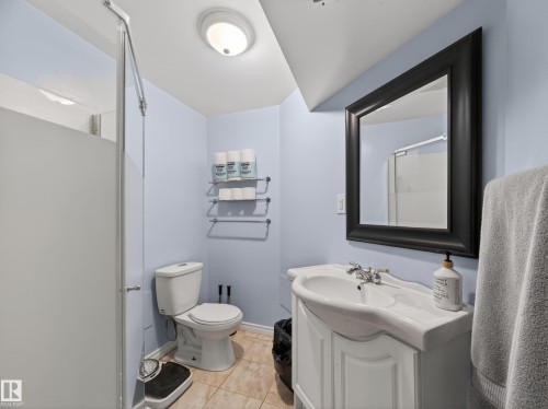 Bathroom featuring a framed mirror, white vanity with integrated sink, toilet, and a shower with a frosted glass panel - 10809 150 Street, Edmonton, AB 