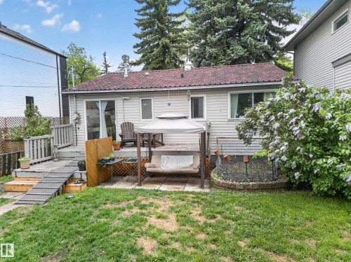 Expansive backyard featuring a manicured lawn, a raised wooden deck with railings and ramp, and a stone-edged garden bed - 10809 150 Street, Edmonton, AB 