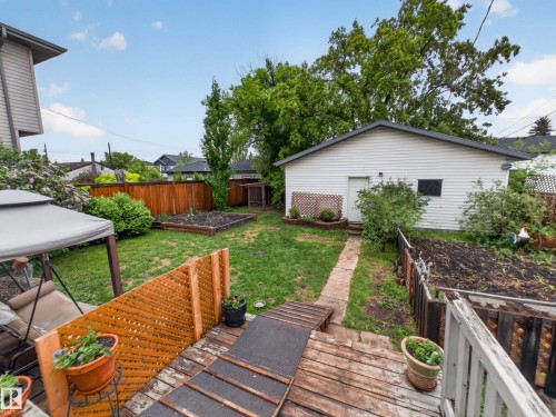 Expansive backyard featuring a detached garage with vinyl siding, a wooden privacy fence, raised garden beds, and a wood-finish deck with privacy lattice - 10809 150 Street, Edmonton, AB 