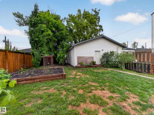 Expansive backyard featuring a raised garden bed, wood fencing, mature trees, and a detached white vinyl-sided structure - 10809 150 Street, Edmonton, AB 