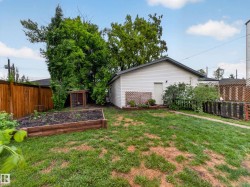 Expansive backyard featuring a raised garden bed, wood fencing, mature trees, and a detached white vinyl-sided structure - 