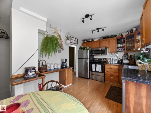 Kitchen featuring wood cabinetry, stainless steel appliances, dark stone-finish countertops, and wood-finish flooring - 10809 150 Street, Edmonton, AB 