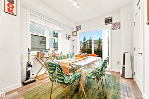 Bright dining space featuring wood-finish flooring, a large window with blinds, and a glass sliding door providing access to an outdoor area - 64 655 Watt Boulevard, Edmonton, AB 